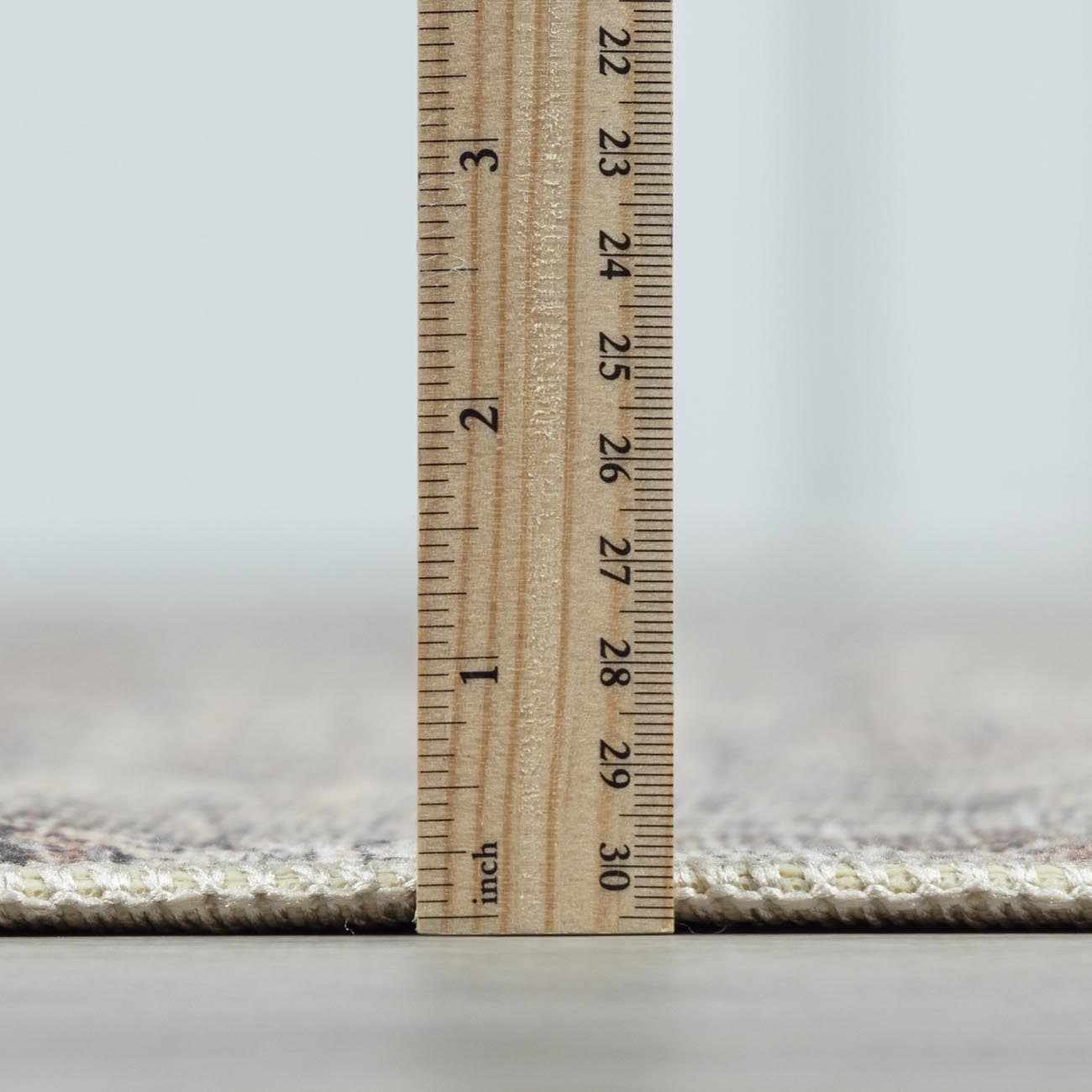 Close-up of the Collins Avenue III Vintage Damask Area Rug showing its pile height with a ruler. Beige, red, green, and ivory colors. Pile
