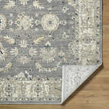Close-up of Noci Ivory Persian rug showing beige, gray, and teal floral pattern and machine-woven texture on wood floor. Fold