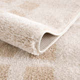 Close-up of the plush Baback Beige Washable Area Rug, showing its soft texture, beige and peach tones, and machine-woven construction. Fold