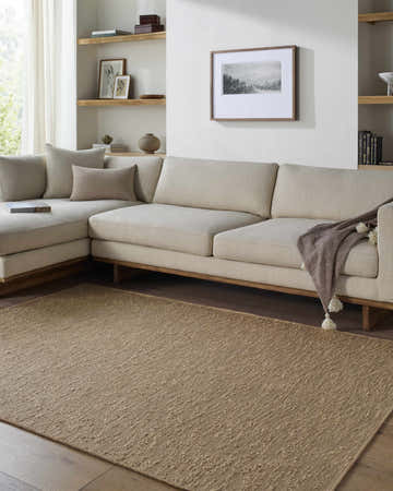 Living room with a sandstone Breena Washable Area Rug, beige sectional sofa, and wood shelving. Roomscene-Rectangle