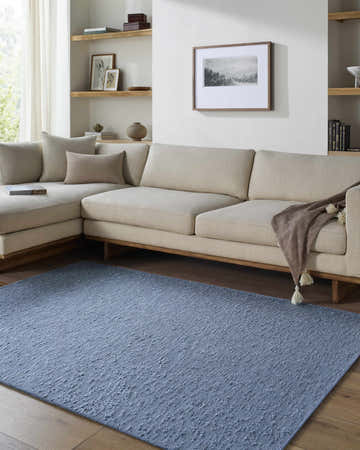 Living room scene with a slate blue Breena Washable Area Rug, beige sectional sofa, and light wood accents. Roomscene-Rectangle