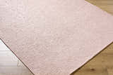 Close-up of the blush Breena Washable Area Rug showing its hand-woven texture and subtle pattern on wood floors. Corner