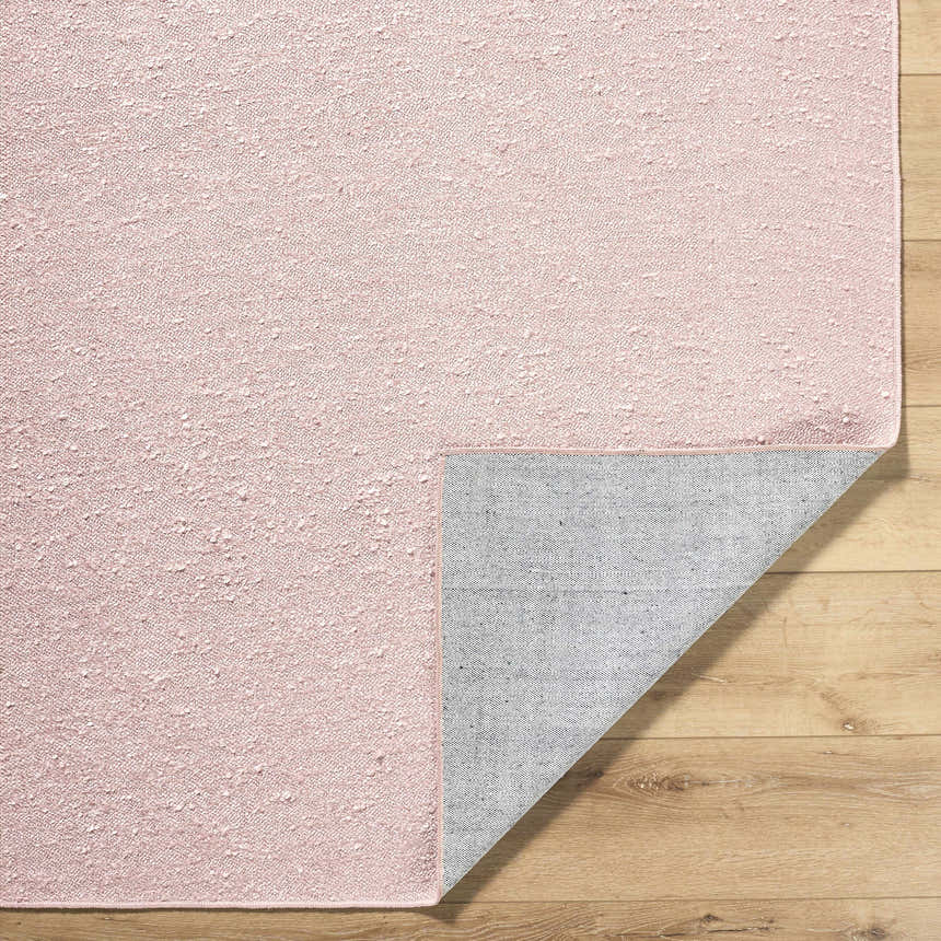 Close-up of the Breena Blush Washable Area Rug showing the textured weave and non-slip backing on a wood floor. Fold