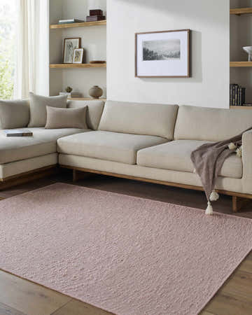 Living room scene with a blush Breena Washable Area Rug, beige sectional sofa, and wood floors. Roomscene-Rectangle