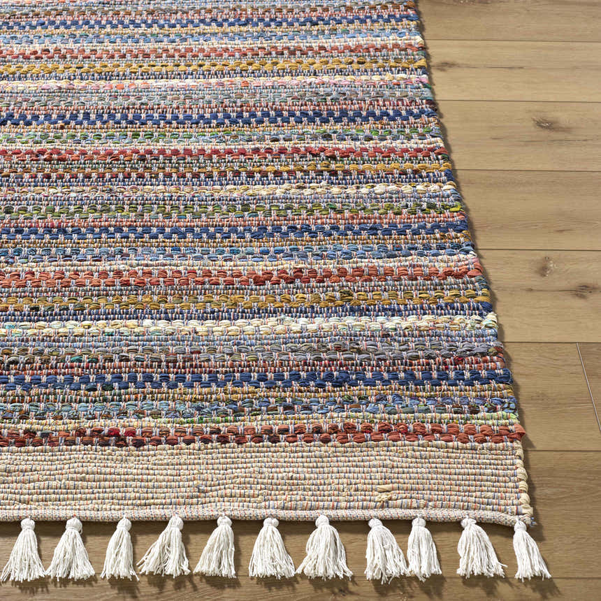 Close-up of the hand woven Brenda Indigo Area Rug. Features indigo, rust, and mustard horizontal stripes and white tassels. Front