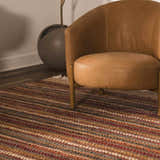 Close-up of the Brenda Indigo Area Rug, a handwoven cotton rug with charcoal, indigo, and rust stripes, styled with a leather chair. Roomscene-Rectangle