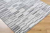 Close-up of Bronco Broken Striped Area Rug. Contemporary design with black, charcoal, gray, ivory, and peach stripes. Corner