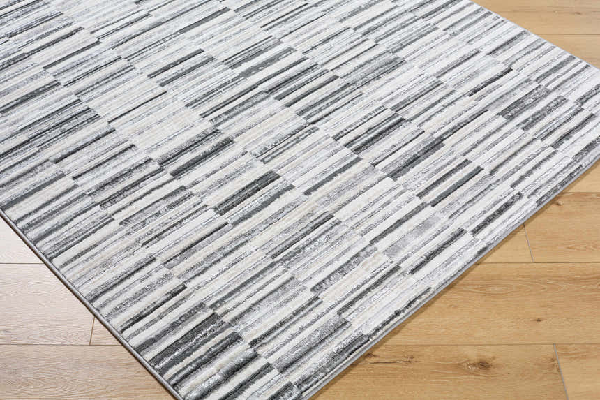 Close-up of Bronco Broken Striped Area Rug. Contemporary design with black, charcoal, gray, ivory, and peach stripes. Corner