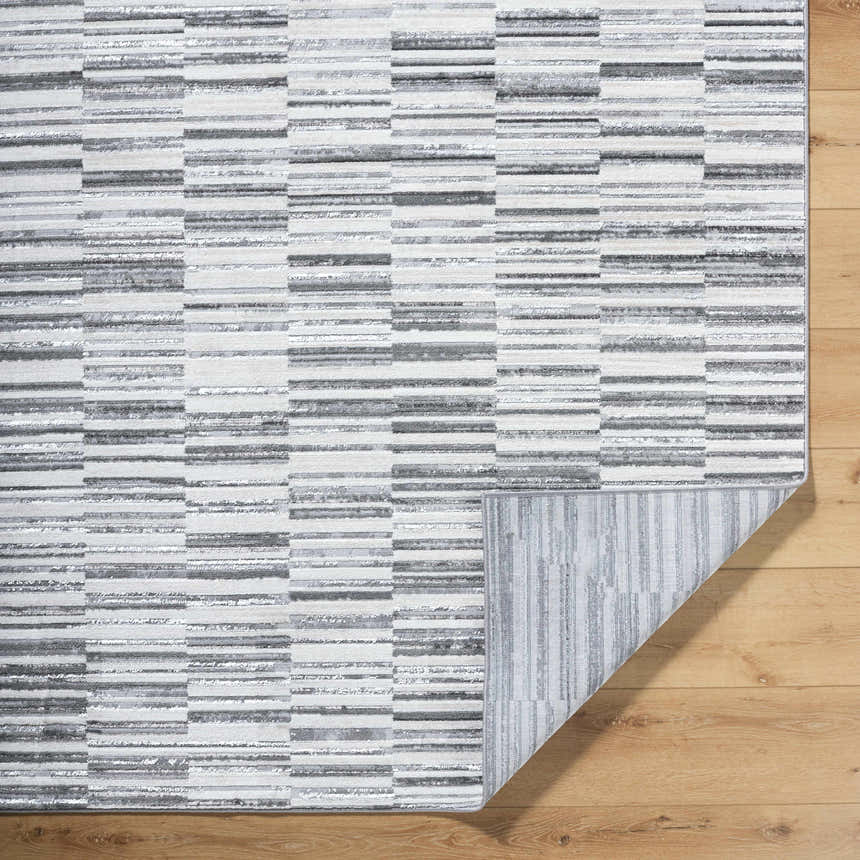 Close-up of Bronco Broken Striped Area Rug. Contemporary design in black, charcoal, gray, ivory, and peach tones. Machine woven texture. Fold