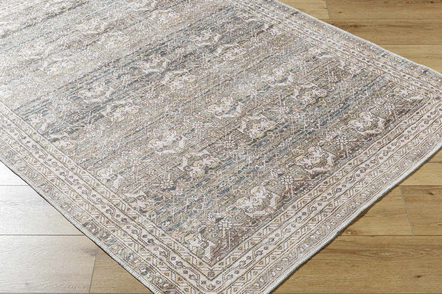 Close up of Billie Vintage Flat Pile Washable Rug on wood floor. Cream, green, and peach traditional rug pattern. Corner