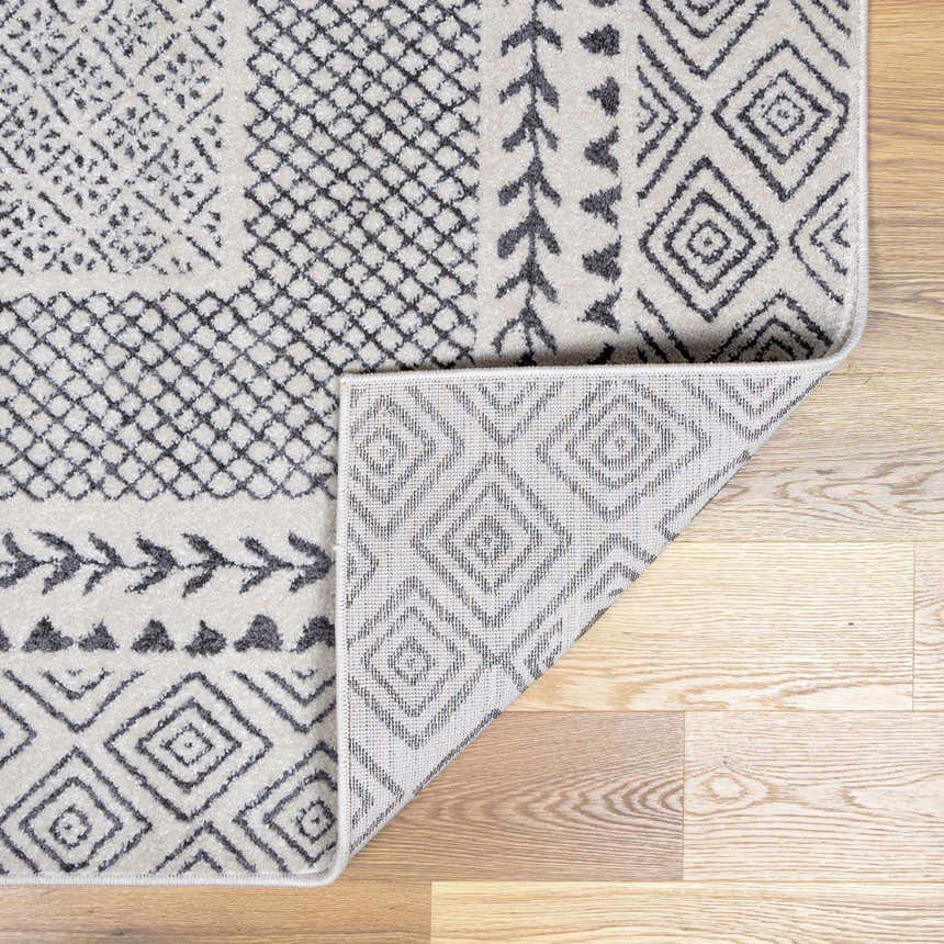 Close-up of the Burdette Soft Neutral Rug featuring charcoal and beige geometric patterns. Machine woven texture. Fold