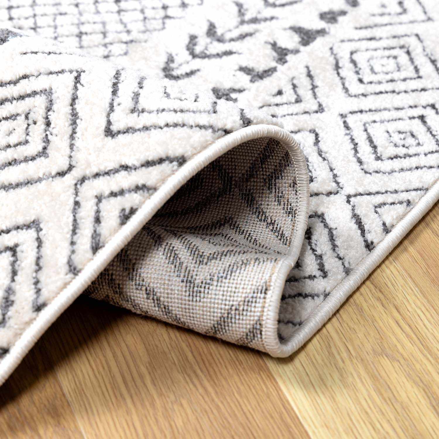 Close-up of the Burdette Soft Neutral Rug showing its geometric charcoal and beige pattern and soft texture. Fold
