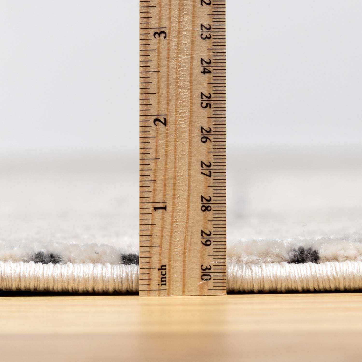 Close-up of Burdette Soft Neutral Rug pile height, showing charcoal and off-white fibers with a ruler for scale. Pile