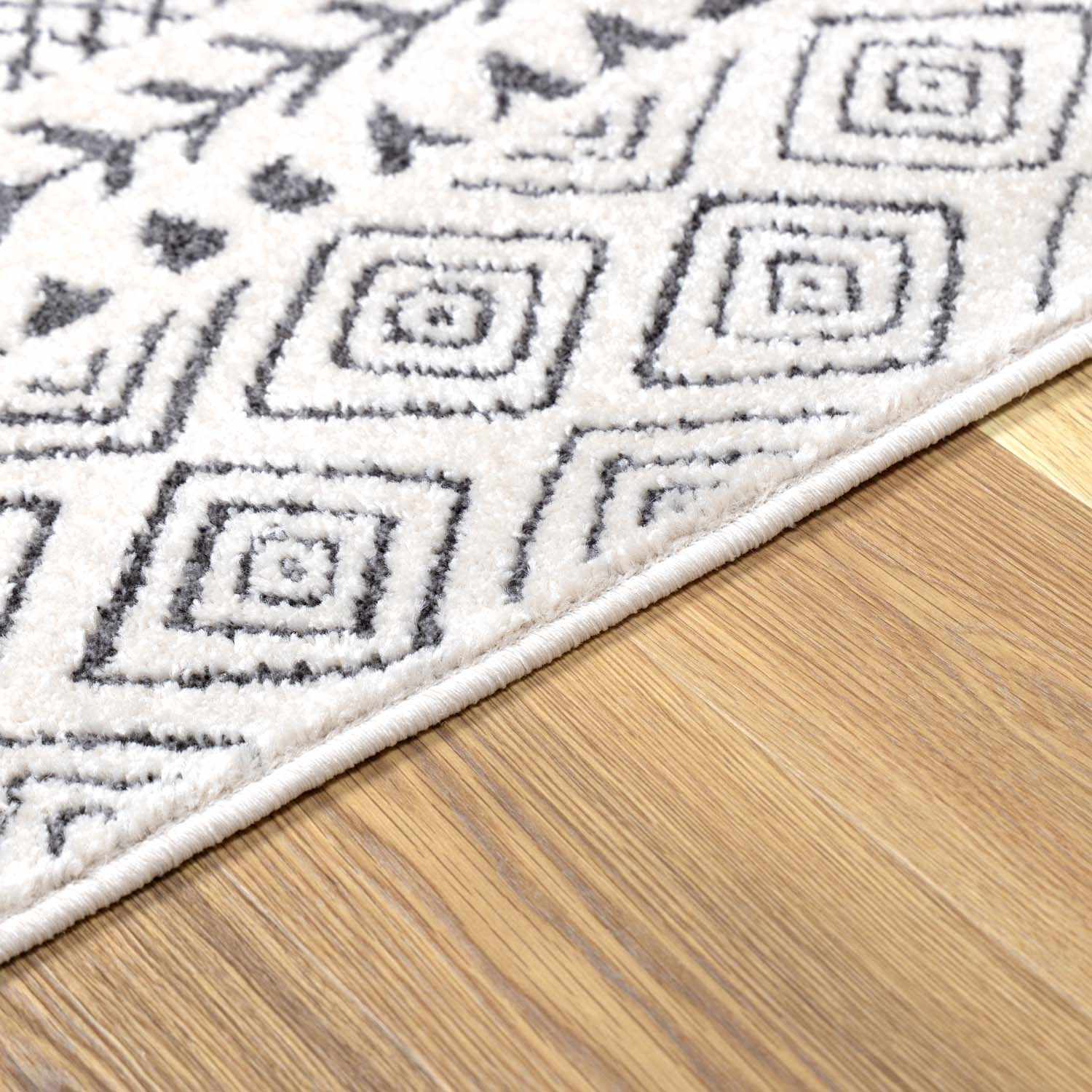 Close-up of the Burdette Soft Neutral Rug with a charcoal geometric pattern on an off-white base. Corner