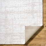 Close-up of the Bianca Area Rug showing its plush white shag texture and durable backing on a light wood floor. Fold