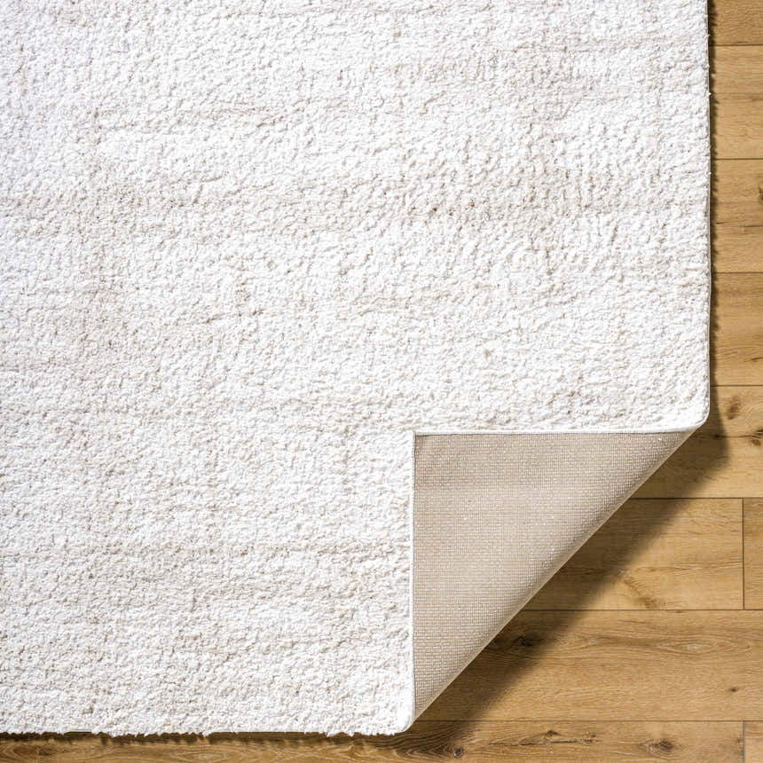 Close-up of the Bianca Area Rug showing its plush white shag texture and durable backing on a light wood floor. Fold