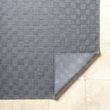 Close-up of the gray Arifah Area Rug showing its woven checkerboard pattern and texture on a light tile floor. Fold