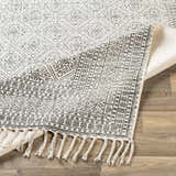 Close-up of the Brushton Area Rug, a beige and black hand-woven cotton rug with a geometric pattern and tassels. Fold