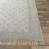 Close-up of the hand woven Brushton Area Rug. Beige cotton rug with black geometric and floral pattern and fringe. Front