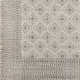 Close-up of the hand-woven Brushton Area Rug. Beige cotton rug with a black geometric diamond and floral pattern. Swatch