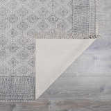 Close-up of Brushton Area Rug with beige cotton backing, black geometric pattern, and fringe on light gray wood floor. Fold