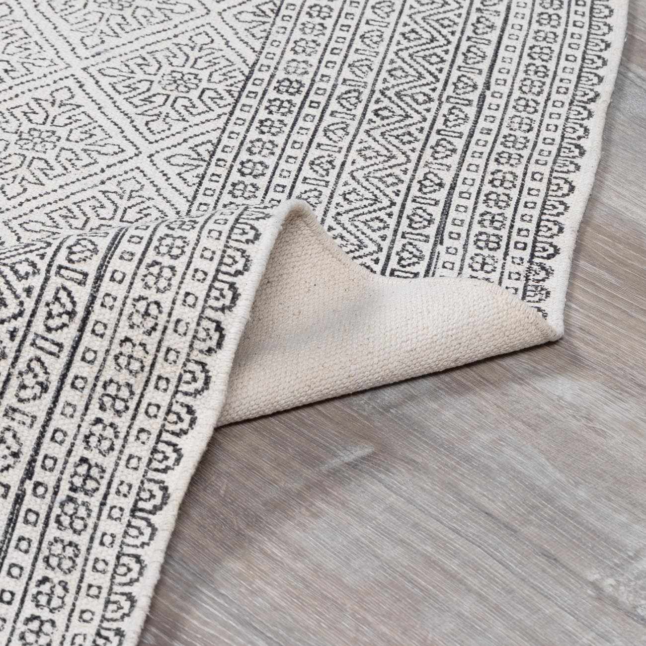 Close-up of the Brushton Area Rug, a hand-woven cotton rug in beige and black with a geometric, bohemian-inspired pattern. Fold