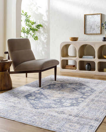 Living room scene with a beige chair on the navy and beige Bethan Washable Area Rug. Neutral decor. Roomscene-Rectangle