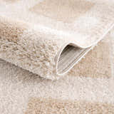 Close-up of the plush texture and beige geometric pattern of the Beynon Beige Washable Area Rug. Fold