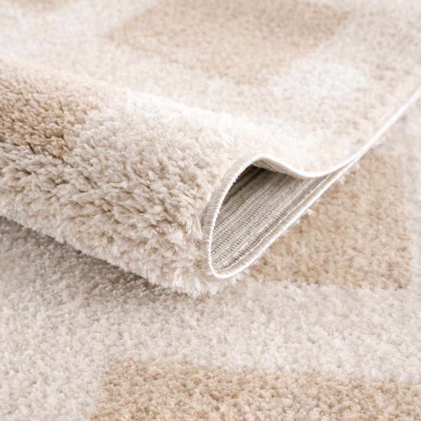 Close-up of the plush texture and beige geometric pattern of the Beynon Beige Washable Area Rug. Fold