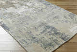 Close-up of the Bued Handmade Wool-Blend Rug. Abstract design in beige, brown, gray, and teal on a wood floor. Corner
