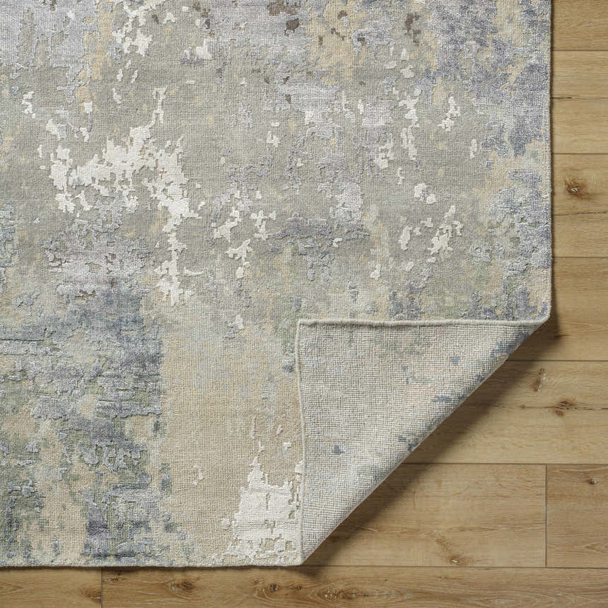 Close-up of the Bued Handmade Wool-Blend Rug. Abstract design in beige, brown, gray, and ivory on a wood floor. Fold