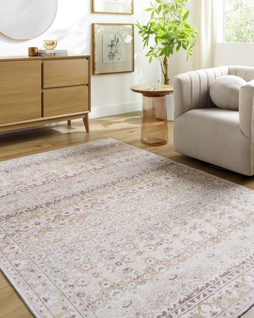 Living room scene with a Bienna Vintage Flat Pile Washable Rug in camel, cream, and brown, styled with a wood dresser and beige chair. Roomscene-Rectangle