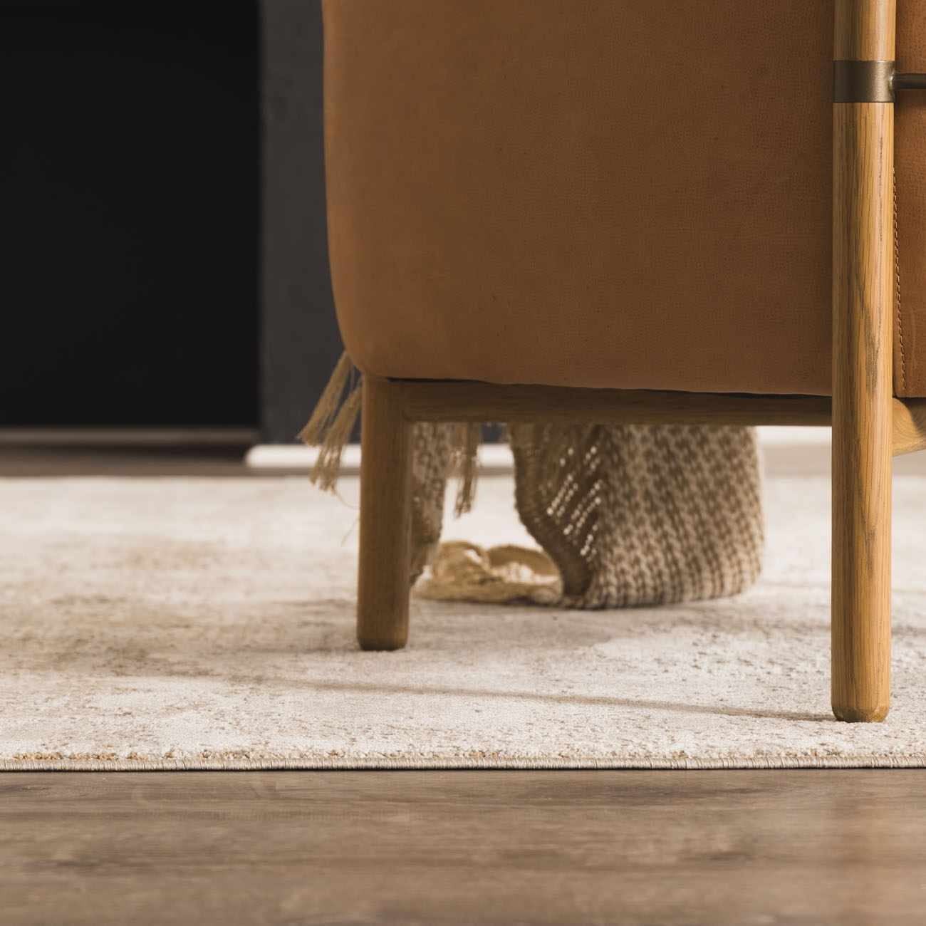 Close-up of the neutral-toned Bowdoinham Thick Luxe Boutique Rug under a tan leather chair on a wood floor. Roomscene-Rectangle