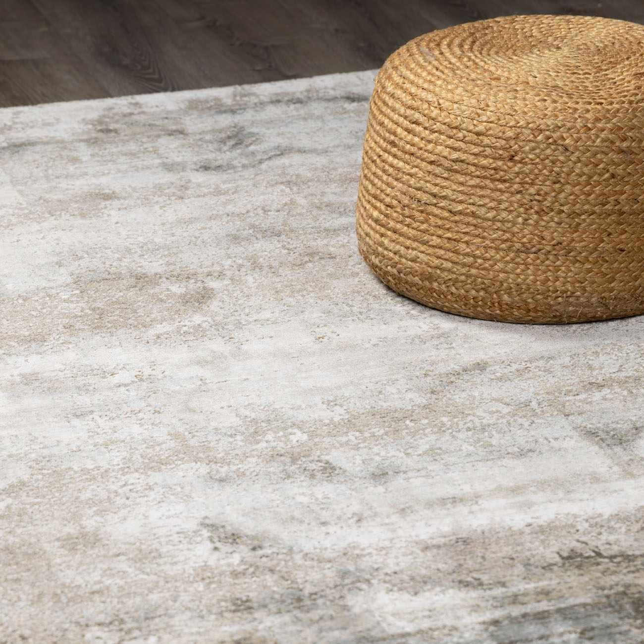Close-up of a Bowdoinham Thick Luxe Boutique Rug in light gray and taupe with a woven jute ottoman. Styleshot