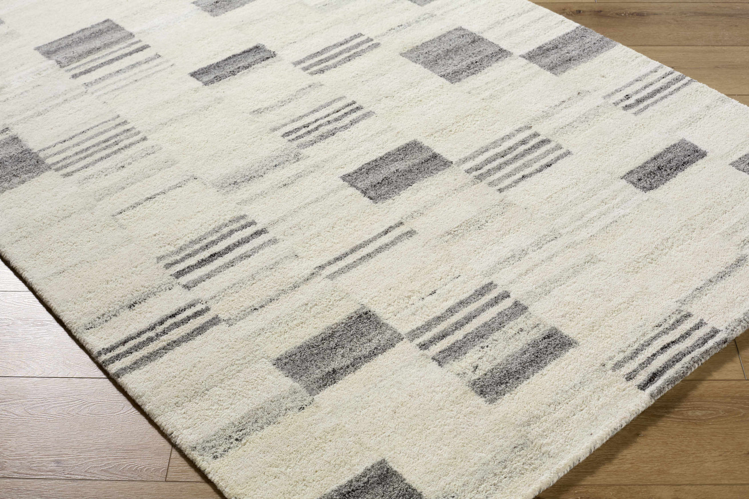 Close-up of the Max Handmade Becki Owens x LIVABLISS BOMX-2305 Area Rug. Cream wool rug with ash, blue, and charcoal geometric pattern. Corner