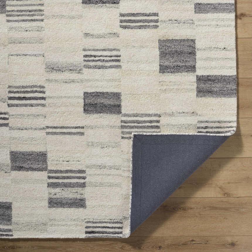Close-up of Max Handmade Becki Owens x LIVABLISS rug. Cream wool rug with ash, blue, and charcoal geometric block and stripe pattern. Fold