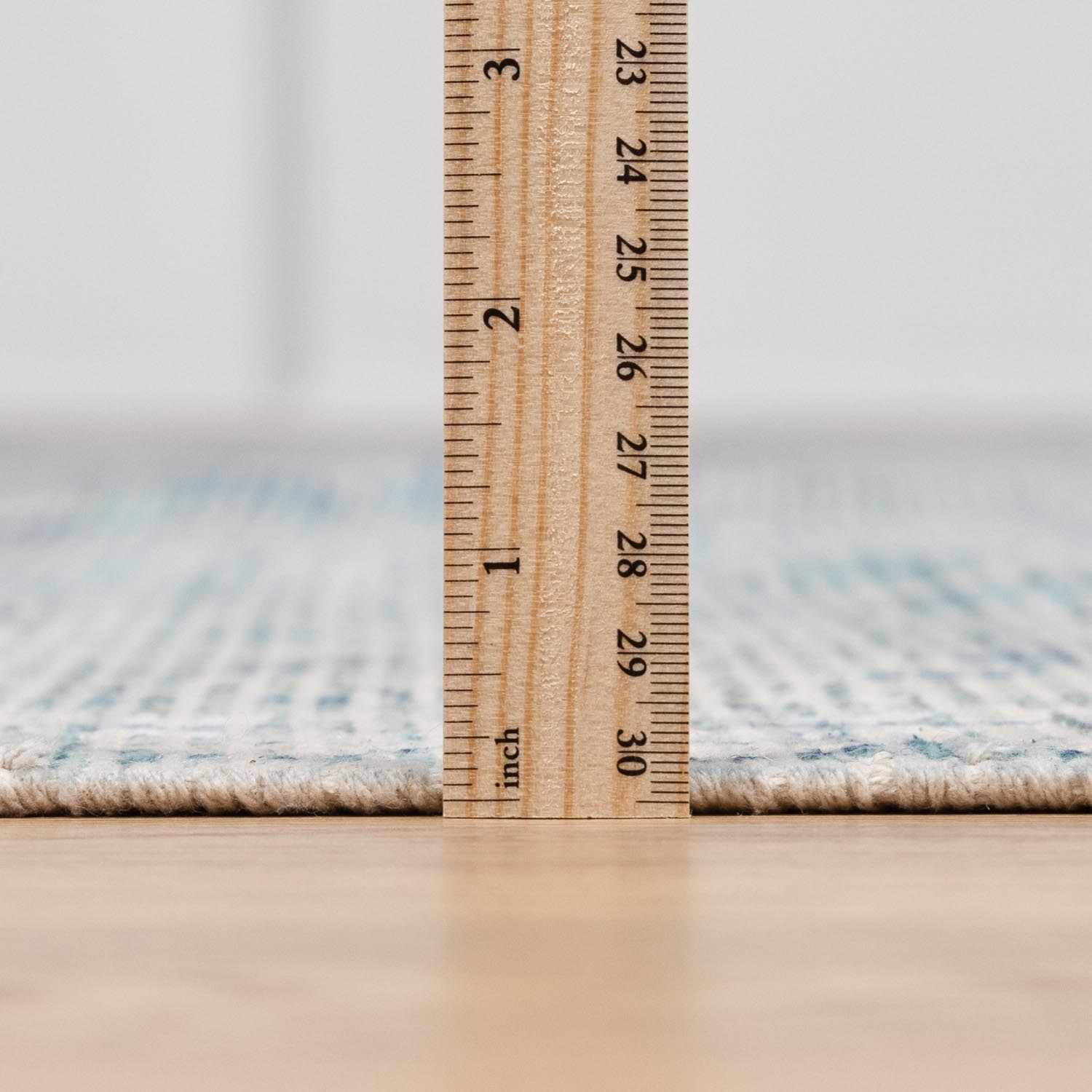 Close-up of the Byers Handmade Cotton-blend Aqua Rug pile height, with a ruler for scale. Aqua and white tones. Pile