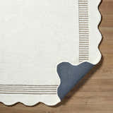 Close-up of the Tono Ivory Border Hand Tufted Wool Area Rug showing the texture, striped border, scalloped edge, and backing. Fold