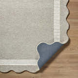 Close-up of Fanae Beige Border Hand Tufted Wool Area Rug showing texture, striped border, and scalloped edge on wood floor. Fold
