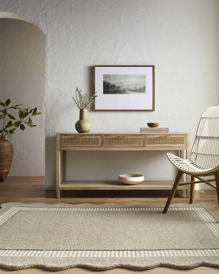 Neutral living room with a Fanae Beige Border rug, console table, and white wicker chair. Roomscene-Rectangle
