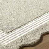 Close-up of the beige, hand-tufted wool Fanae rug with a striped border on a wood floor. Texture
