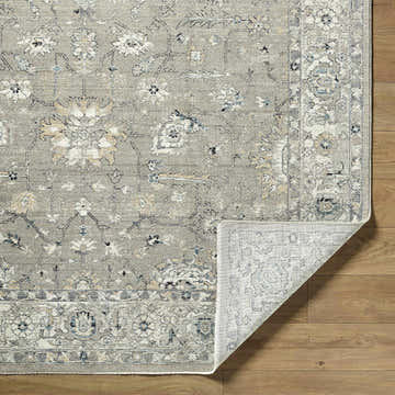 Close-up of the Briony Area Rug showing its traditional floral pattern in gray, white, and blue on a wood floor. Fold