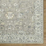Close-up of a Briony Area Rug showing a traditional floral pattern in shades of gray, white, and blue on a wood floor. Corner