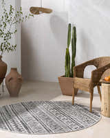 Modern patio scene with a round black and white Catrine Indoor Outdoor Rug, wicker chair, and cacti. Roomscene-Round