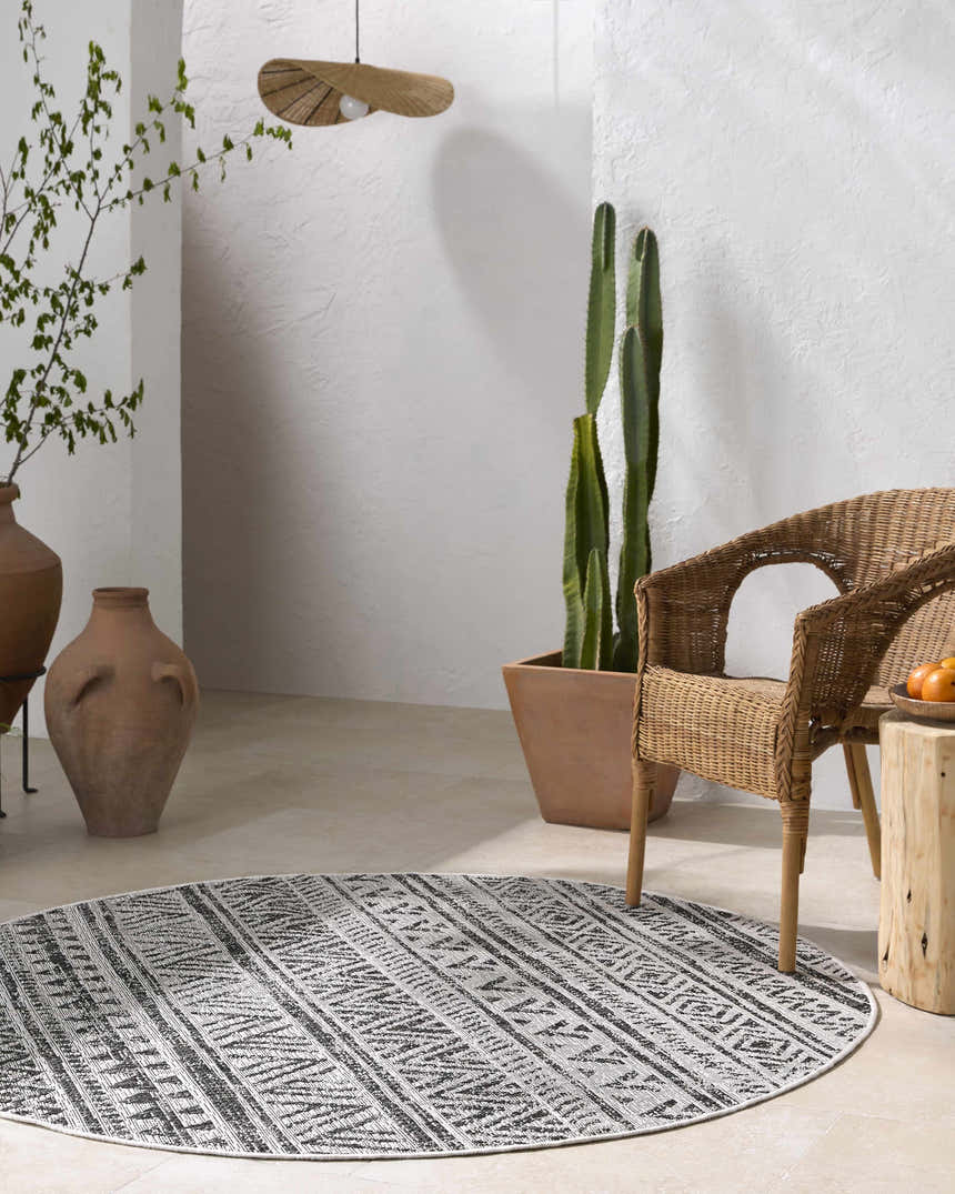 Modern patio scene with a round black and white Catrine Indoor Outdoor Rug, wicker chair, and cacti. Roomscene-Round