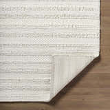 Close-up of the hand-woven Coskun Area Rug. Features a textured, looped pile design in creamy white wool on wood floors. Fold