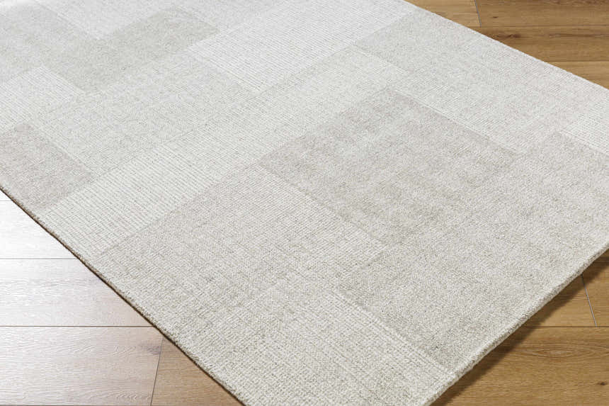 Close-up of the beige Camila Area Rug, a hand-tufted wool rug with a subtle geometric pattern on wood floor. Corner