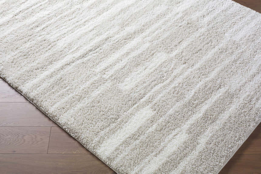 Close-up of the ivory and peach Carlen Area Rug, a soft shag rug with subtle stripes, on a wood floor. Corner