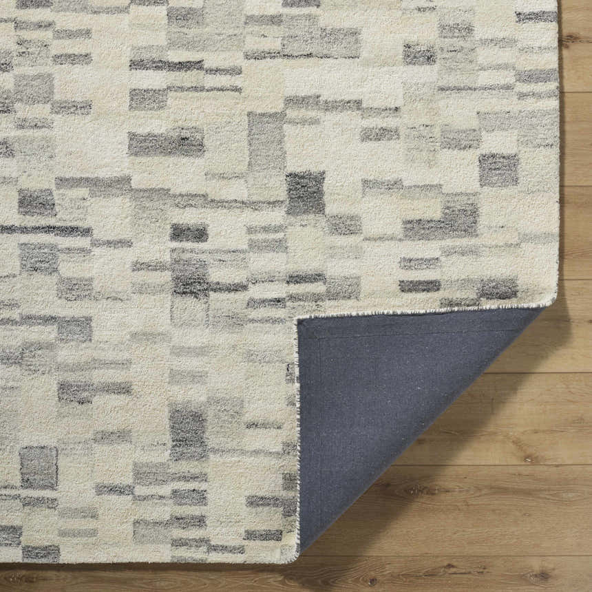 Close up of the Max Handmade Becki Owens x LIVABLISS rug, featuring a geometric pattern in ivory, dove gray, charcoal, and blue. Fold