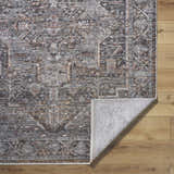 Close-up of the Clovia Area Rug showing its traditional black, gray, ivory, and brown pattern and texture on wood floor. Fold